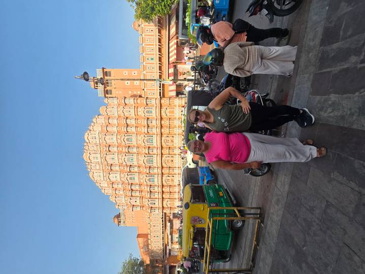 Travellers pose on busy street with the ornate façade of Jaipur’s Hawa Mahal rising behind