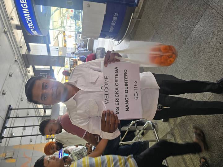 Airport greeter holds a printed welcome sign with passenger names in busy arrivals hall