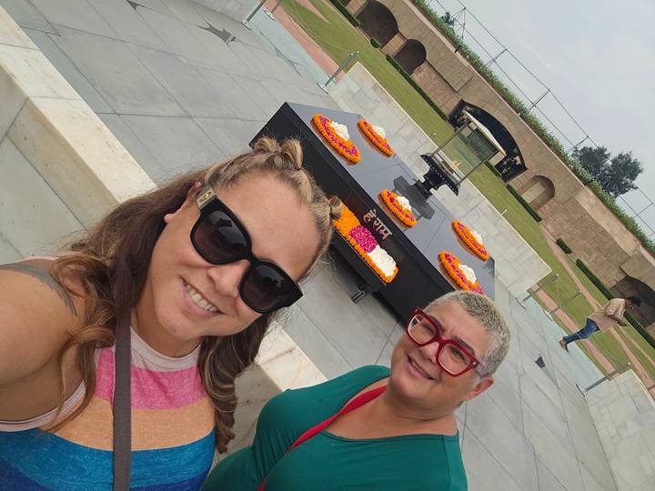 Selfie of two travellers in front of the black granite Gandhi memorial adorned with flower wreaths