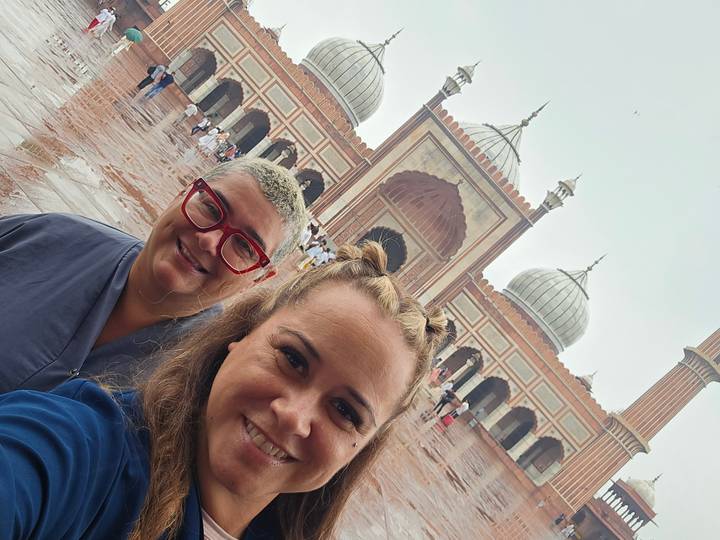 Selfie of two travellers in front of Jama Masjid’s grand domes on a wet courtyard day