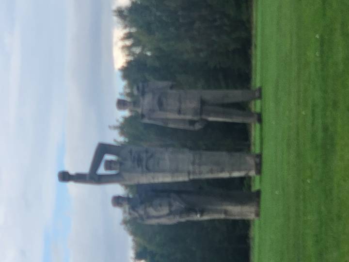 Three large concrete Soviet-era statues standing in a grassy park.