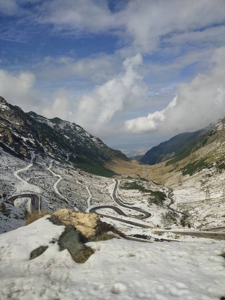 Winding Transfagarasan mountain road snakes through snow-dusted Romanian peaks toward distant plains.