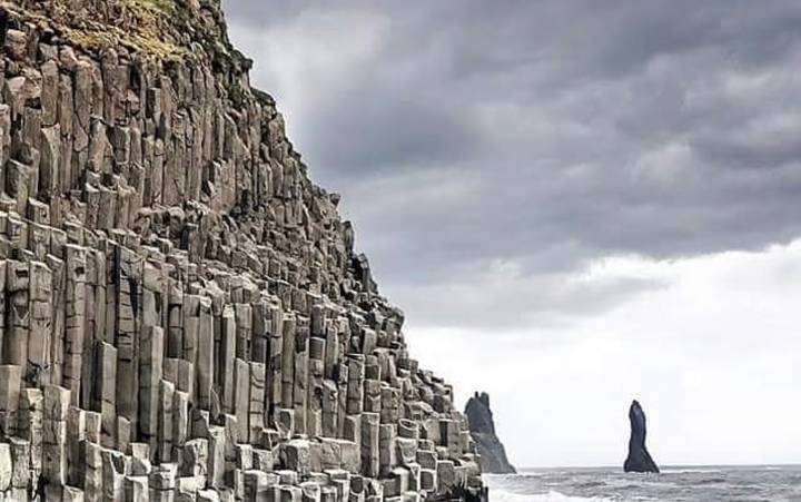 Sheer basalt column cliffs meeting grey North Atlantic waves under dramatic overcast sky.