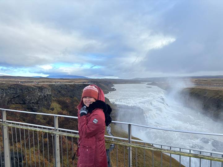 Woman in winter clothing standing at railing overlooking the powerful Gullfoss waterfall amid mist.