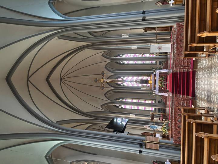 Neo-Gothic church interior with high vaulted arches, stained glass windows and ornate altar.