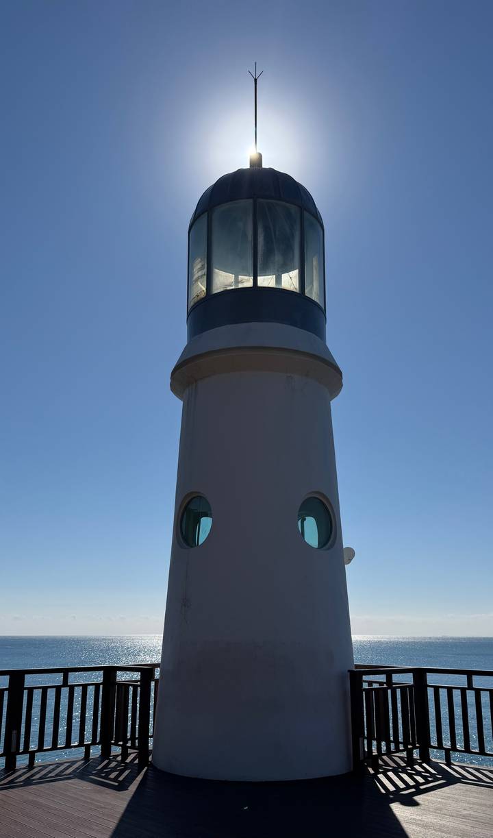 Tall white lighthouse set against a clear blue sky viewed from ground level.