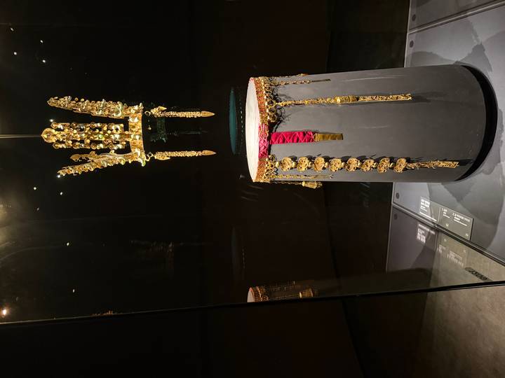 Ancient golden crown displayed inside a dark glass case at a museum exhibit.