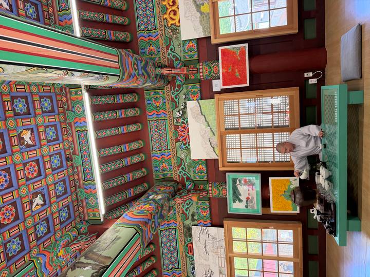 Monk prepares traditional tea inside a vividly painted Korean temple interior lined with artwork.