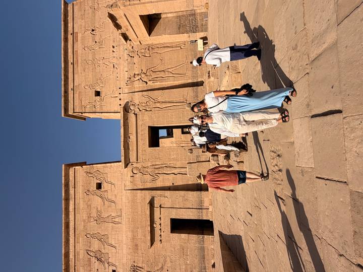 Visitors walking across the stone courtyard of an ancient Egyptian temple with detailed reliefs