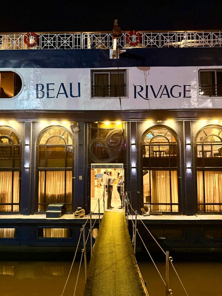 Night view of a Nile cruise ship façade with arched windows lit warmly and the name Beau Rivage
