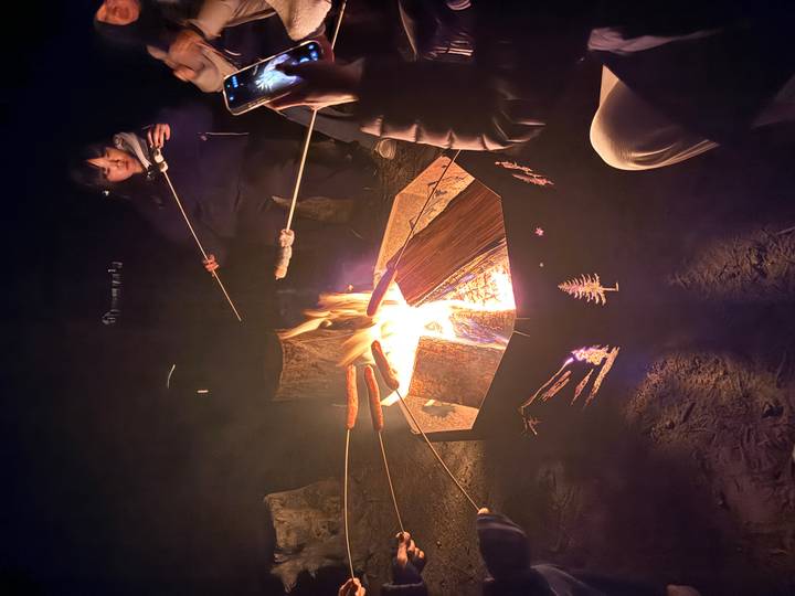 Campfire at night with travelers roasting marshmallows and sausages over open flames