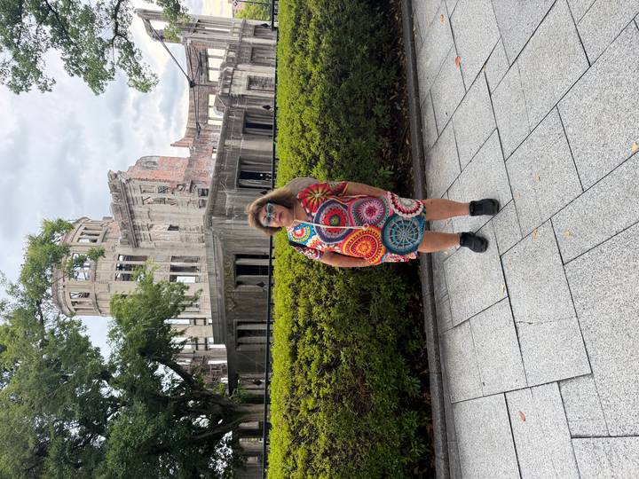Person posing in front of the ruined Atomic Bomb Dome surrounded by greenery.