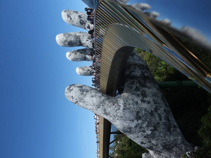 Crowds walk across Da Nang’s iconic Golden Bridge, held aloft by giant stone hands under a clear blue sky.