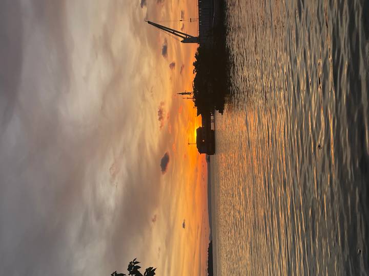 A fiery sunset paints the sky over calm coastal waters and a small pier.