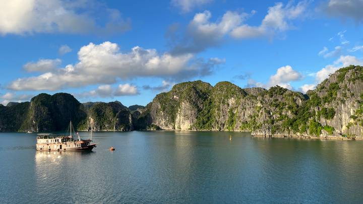 A traditional junk boat anchors amid the tranquil karst islands of Halong Bay under blue skies.
