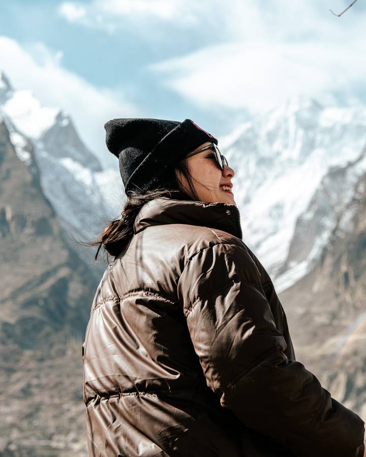Close-up portrait of a smiling traveller wearing a beanie with towering snowy mountains behind.