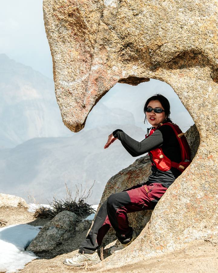 A hiker framed by a natural rock arch gestures playfully with misty mountain vistas beyond.