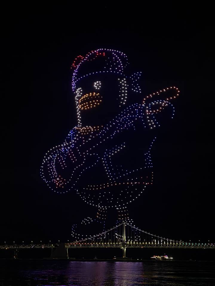 Night drone light show forming an animated bear playing guitar with bright dots.