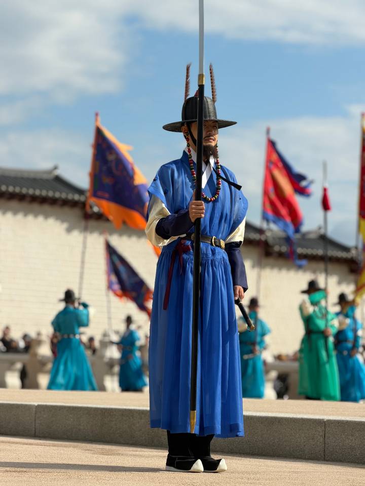 Palace guard in vivid blue robe holds a spear during traditional changing-of-guard ceremony.