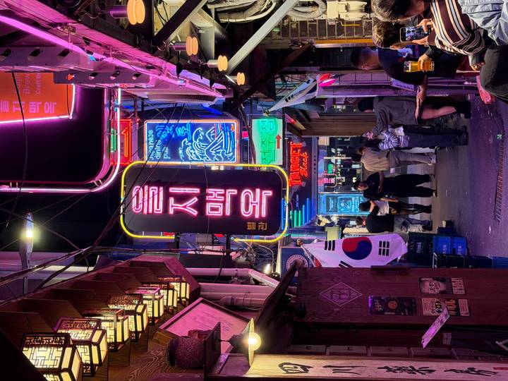 Vibrant neon alley in a Korean nightlife district with people socialising beneath the lights.