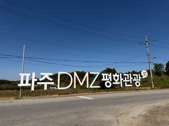Large roadside sign for the Paju DMZ Peace Tourism area against a clear blue sky.