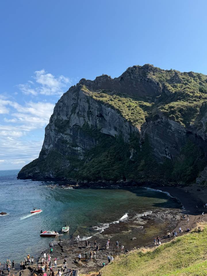 Steep green cliff rising from the ocean with a partly cloudy blue sky.