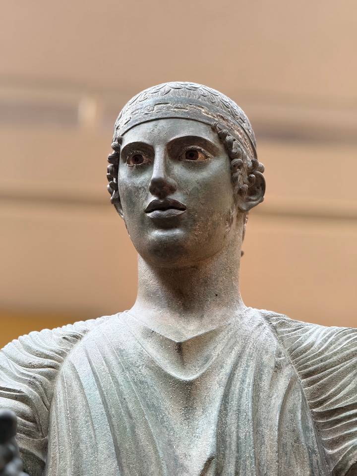 Close-up of the bronze Charioteer of Delphi statue with soft museum lighting.