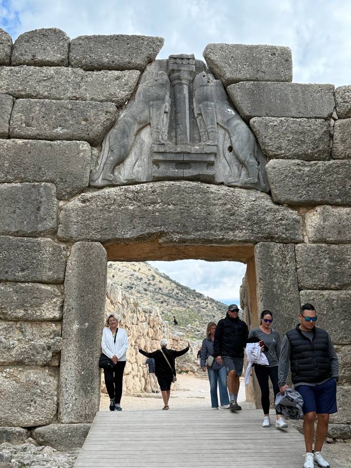 Visitors stand beneath the Lion Gate entrance of ancient Mycenae with carved stone lions above.