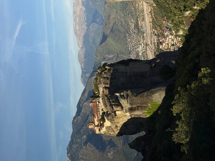 Monastery perched atop a massive rock pillar in the Meteora region with mountains in the background.