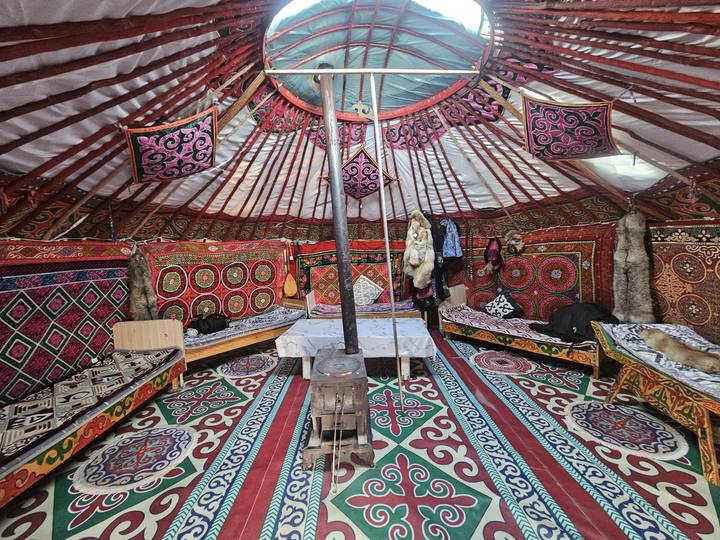 Color-saturated interior of a Kazakh ger decorated with patterned carpets, tapestries and saddles.
