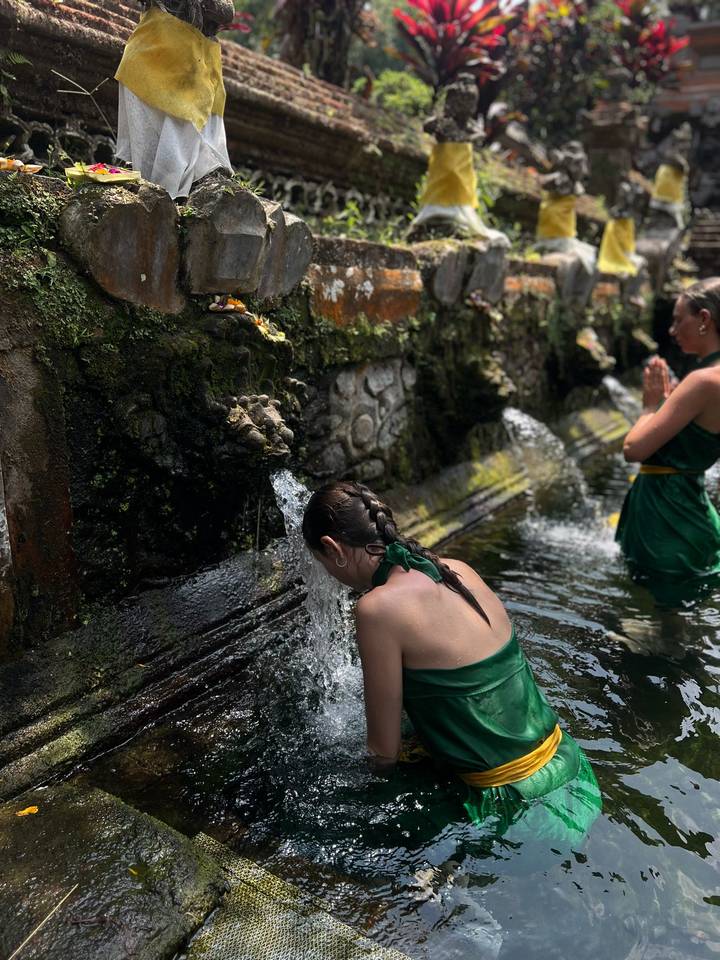 Women dressed in green sarongs take part in a purification ritual under stone spouts at a Balinese water temple.