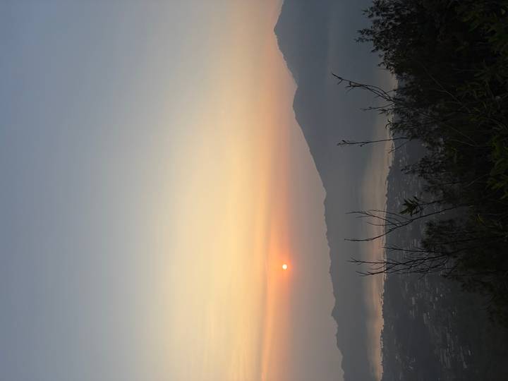 Serene sunrise over a misty lake and volcanic mountain ridge, viewed from a hillside.