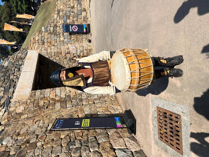 Costumed performer in traditional armor holds a drum outside fortress walls at a heritage event.