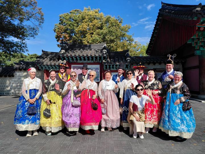 Large tour group wearing colorful hanboks posing in front of traditional Korean palace gate.