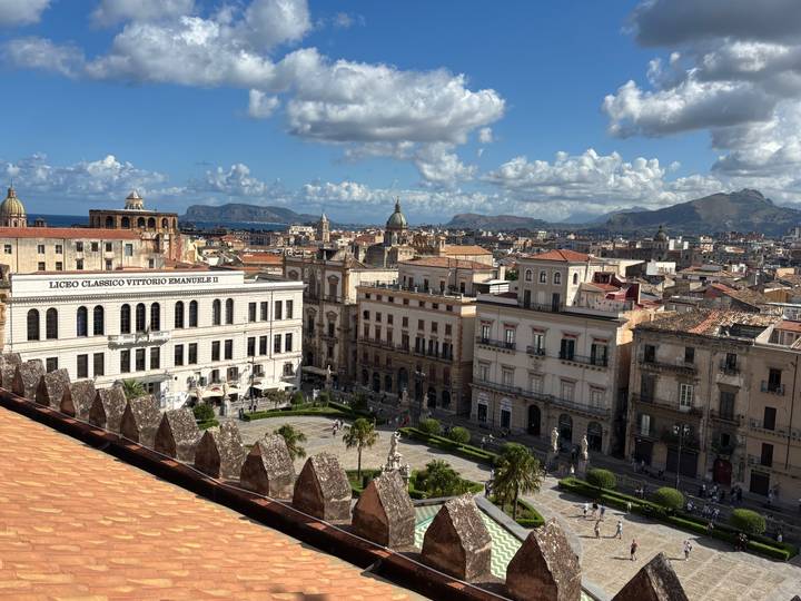 Panoramic rooftop view over Palermo's historic center with domes, piazzas and distant mountains beyond the bay.