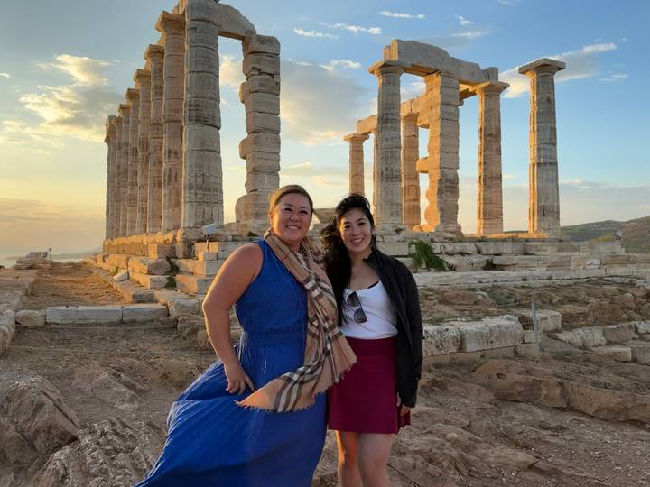 Two friends pose before the ancient columns of the Temple of Poseidon bathed in golden evening light.