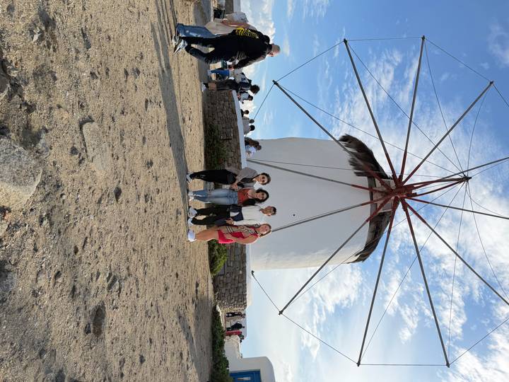 Group of travellers standing before the famous white windmill on Mykonos under a bright blue sky.