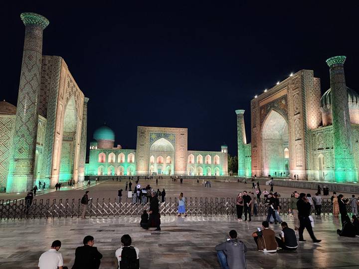 Illuminated Registan Square with its magnificent madrasas glowing green against the night sky.