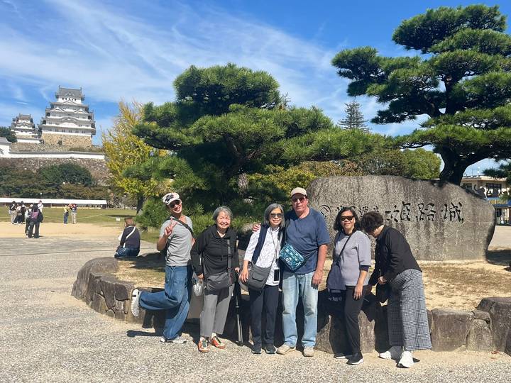 Small tour group poses in front of Himeji Castle and landscaped pines on a sunny day.