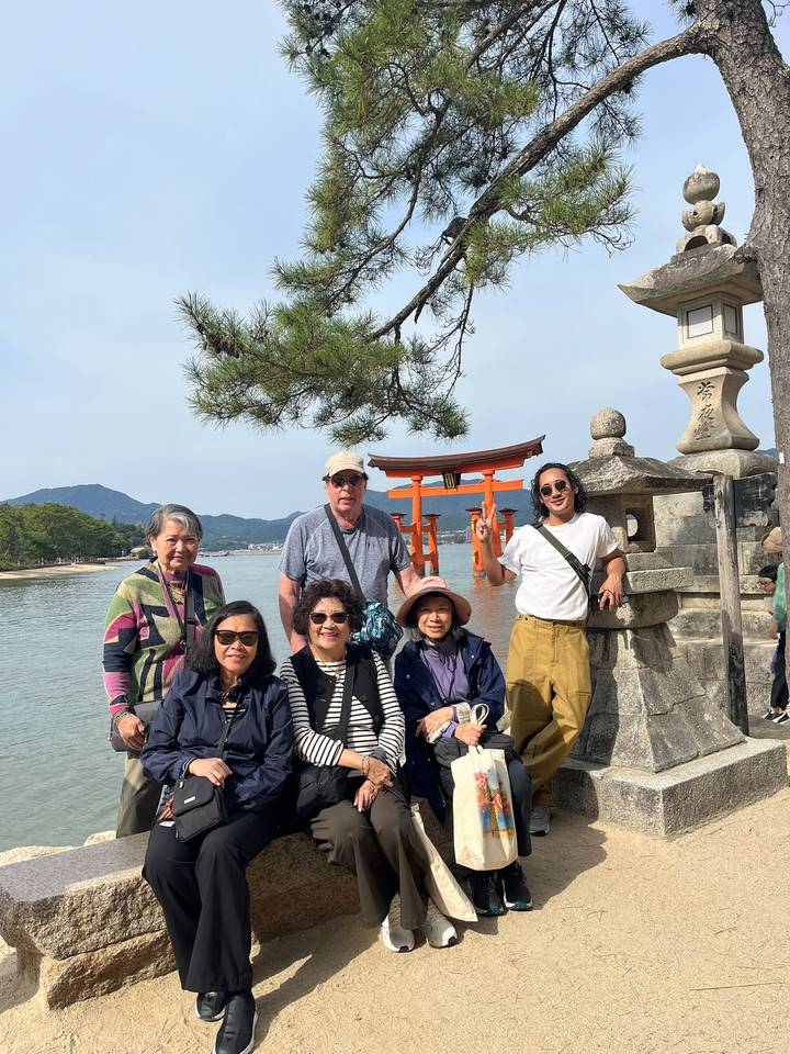 Group poses by Miyajima’s famous floating torii gate beside a stone lantern.
