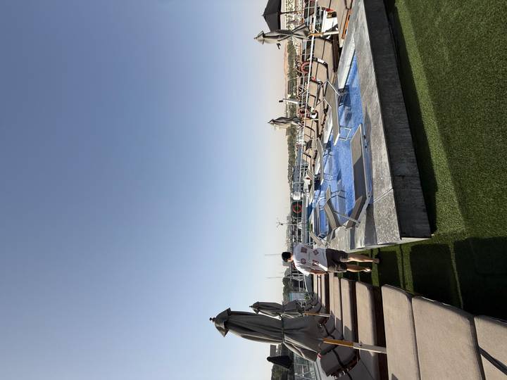 Rooftop pool deck on a Nile cruise ship with sun-loungers, umbrellas and a passenger walking alongside.