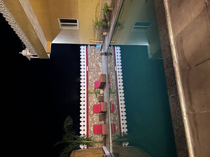 Outdoor swimming pool at night with cushioned loungers reflected in calm water