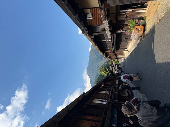 Traditional wooden houses line a quiet mountain village street under a clear blue sky.