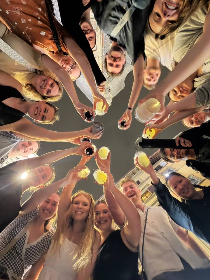 Travel companions raise drinks in a celebratory nighttime toast captured from below.