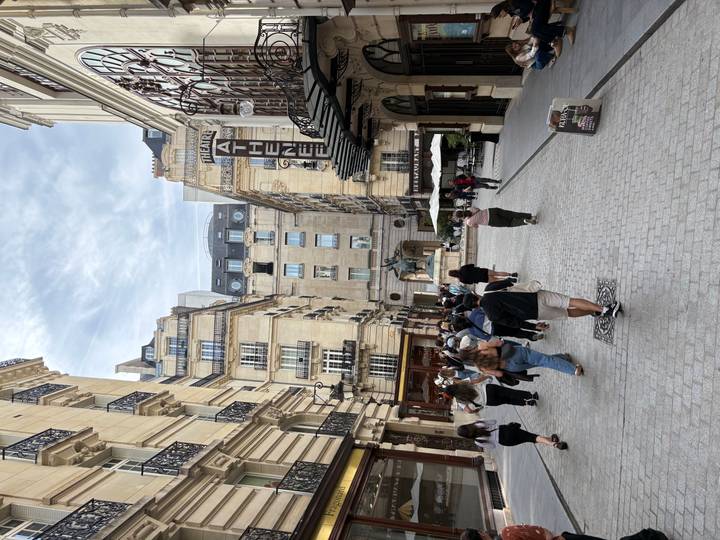Tourists walk through a charming Parisian pedestrian street lined with classic limestone buildings and cafés.