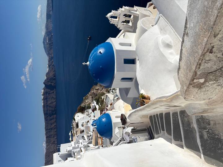 Iconic blue-domed church rooftops and whitewashed houses cascade to deep blue Aegean Sea in Oia.