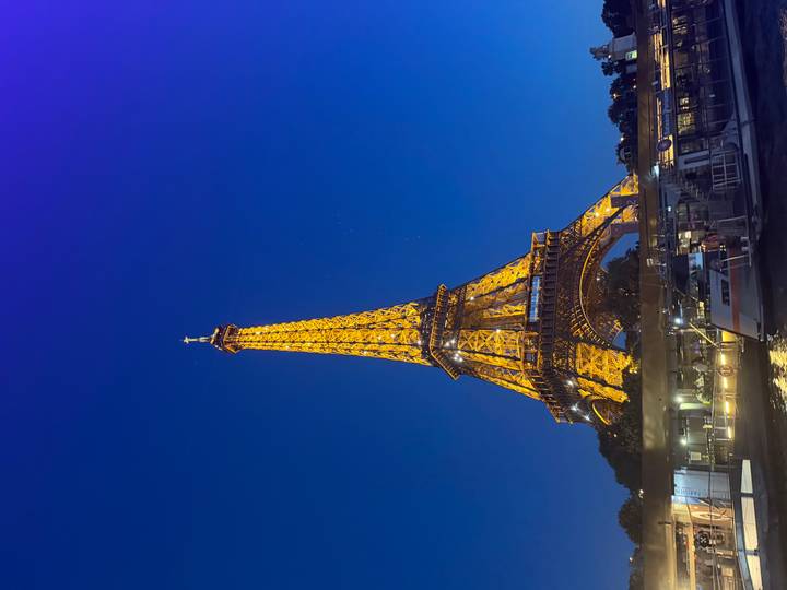 The Eiffel Tower glows golden against a deep blue night sky with river boats below.