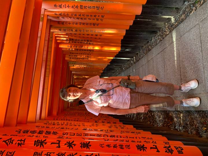 Smiling traveller standing in the famous tunnel of vermilion torii gates at Fushimi Inari Shrine.