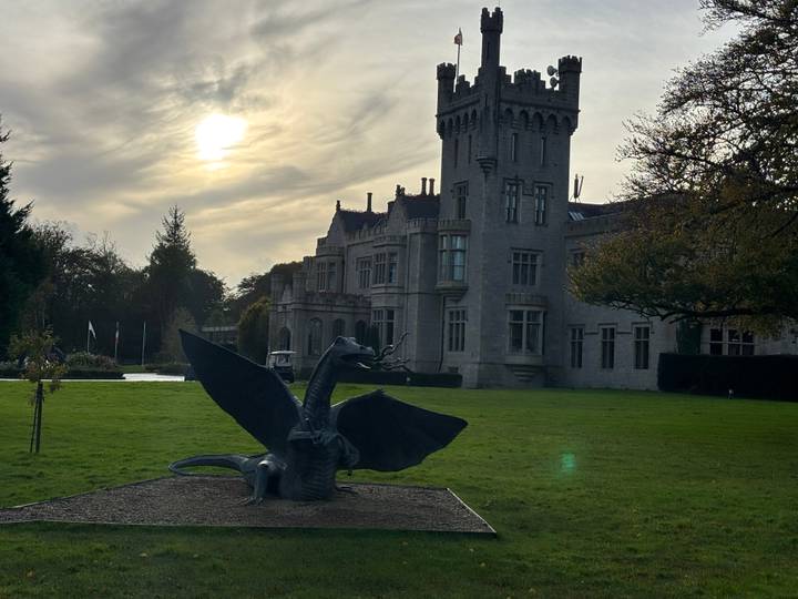 Stone castle with dragon sculpture on the lawn silhouetted by a hazy afternoon sun.