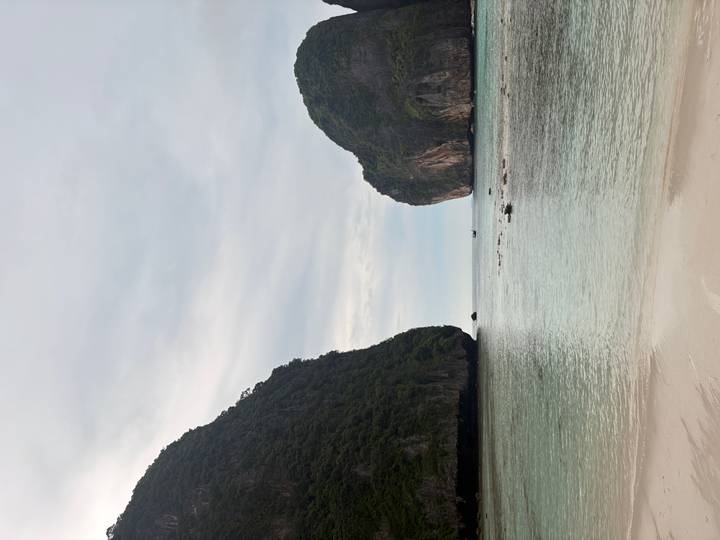 Serene beach cove framed by two towering limestone cliffs on an overcast day with gentle turquoise water.